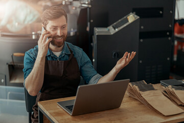 Business owner of small coffee roasting factory talking phone on his workplace