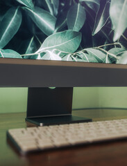 Close up of white keyboard and large screen on wooden desk with green backlighting