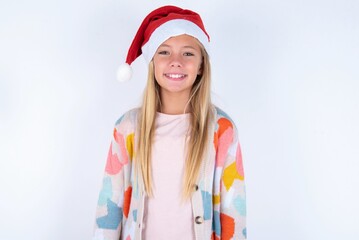 little kid girl with Christmas hat wearing yarn jacket over white background with a happy and cool smile on face. Lucky person.
