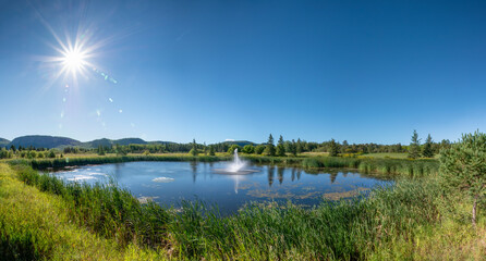 A fountain spouts water in the center of a pond, basking in the bright morning sun in Thunder Bay, Ontario.