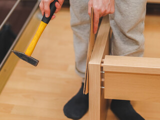 Caucasian young man hammers wooden nails with a yellow hammer