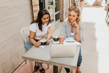 Two professional females work on computer together over coffee