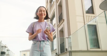 Asian woman in earphones enjoys listening to music in street