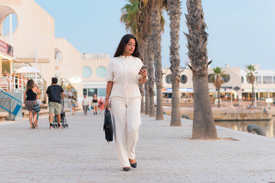 Elegant woman with a briefcase walks around looking at her phone