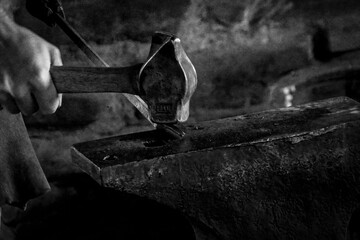 A blacksmith swings a hammer against a hot piece of metal on an anvil at Fort William, a former fur...