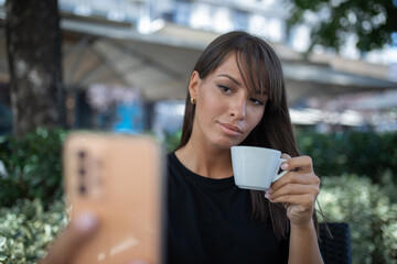 Morning in cafe - attractive woman in black drinkin coffe and make selfie photo for social networks