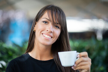 Beautiful smiling woman drinking coffee in garden of cafe