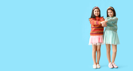 Cute little sisters holding hands together on light blue background with space for text