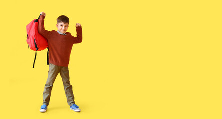 Fototapeta premium Little schoolboy holding backpack on yellow background with space for text