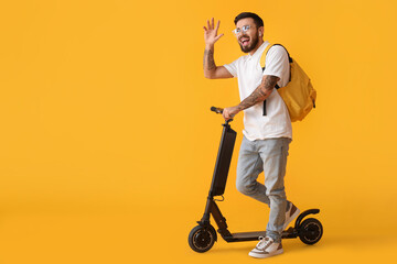 Handsome tattooed student with kick scooter on yellow background © Pixel-Shot