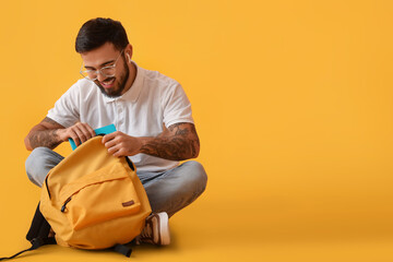 Handsome tattooed student with backpack on yellow background