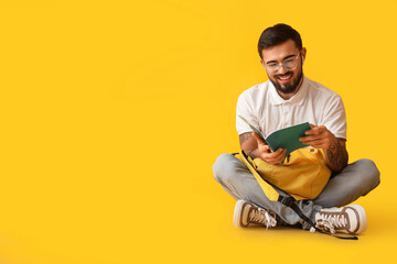 Handsome tattooed student with backpack on yellow background