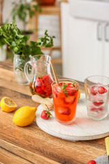 Tray with glass of cold strawberry lemonade on table in kitchen