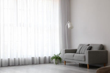 Interior of light living room with grey sofa, standard lamp and houseplant