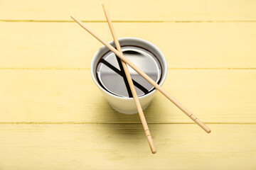 Bowl of soy sauce and chopsticks on yellow wooden background