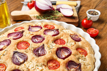 Baking dish of tasty Italian focaccia with vegetables on wooden table, closeup
