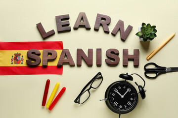 Text LEARN SPANISH, stationery, flag, alarm clock and eyeglasses on beige background