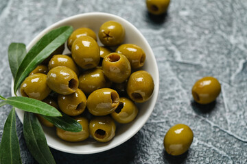 Bowl of delicious green olives on dark color background, closeup