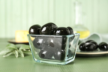 Glass bowl with tasty black olives on color wooden table