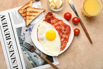Plate with tasty fried egg, bacon, toasts, glass of juice and newspaper on color background