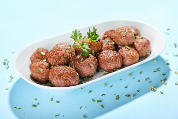Plate with tasty meat balls and herbs on blue background