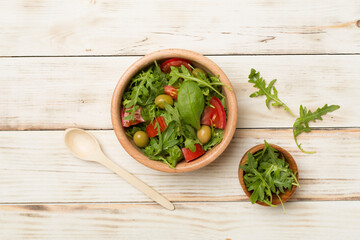 Fresh salad with arugula, spinach and vegetables on wooden background, top view