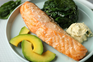 Tasty salmon with spinach and avocado on plate, closeup
