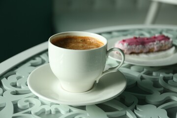 Cup of delicious aromatic coffee and eclair on table indoors