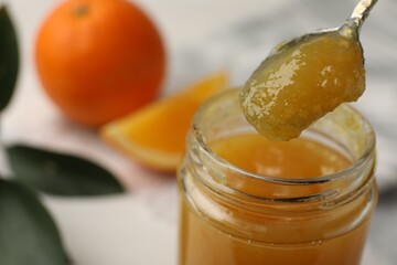 Spoon and jar with delicious orange marmalade on table, closeup. Space for text