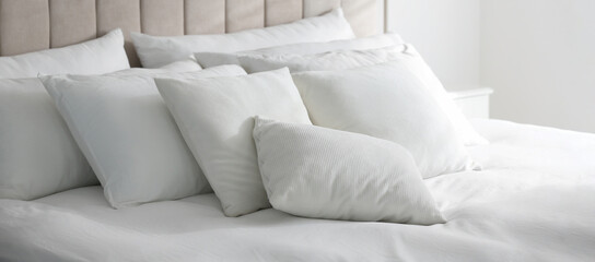 Comfortable bed with soft white pillows indoors. Banner design
