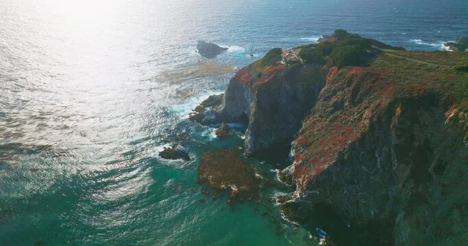 Flying closer to the mansion locating on the tor of the rocks at California coastline. Pacific ocean splashing waves by the rugged shore. Aerial view.