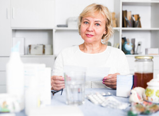 Mature woman sits at the table with medicines and bills for treatment