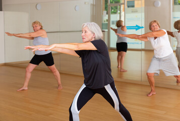 Fototapeta na wymiar Portrait of athletic european aged woman doing stretching warm-up during group workout at gym .