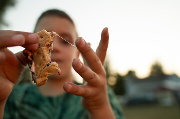 boy eating smore with marshmallow sticking to his fingers at a summer campfire