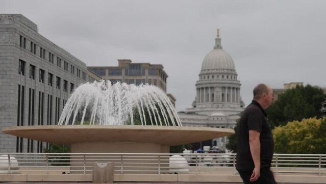 Caucasian male in black clothes walking in front of water fountain at Monona Terrace in Madison, Wisconsin in slow motion.