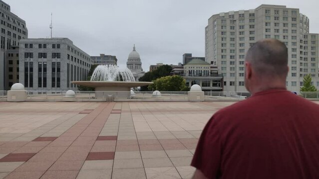 Caucasian male in maroon shirt walking to camera on the Monona Terrace in Madison, Wisconsin with gimbal video behind.