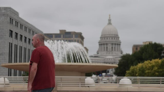 Caucasian male walking in front of water fountain at Monona Terrace in Madison, Wisconsin in slow motion.