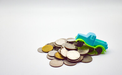 A blue-green pickup truck climbs on a pile of coins on a white background.