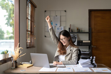 Successful young asian business woman achieving goals excited raised hands rejoicing with laptop on...