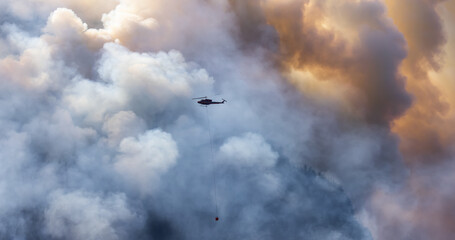 Wildfire Service Helicopter flying over BC Forest Fire and Smoke on the mountain near Hope during a hot sunny summer day. British Columbia, Canada. Natural Disaster