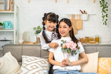 Obraz na płótnie Canvas Attractive beautiful asian mum sitting on sofa . daughter give gift box and flower in family moment.Women's or Mother's day or birthday, sitting on sofa.