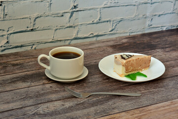 A plate with a slice of cheesecake Belgian cream with mint leaves and a cup of hot black coffee on a wooden table.