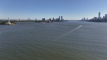 An aerial view of New York Harbor on a sunny day with clear blue skies. The drone camera truck right viewing the Statute of Liberty, New Jersey and lower Manhattan in the background.
