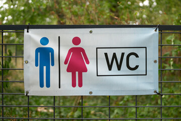 Hinweis auf eine in der Nähe befindliche Toilette durch ein Schild an einem Zaun in einem Park in Deutschland - 530207272