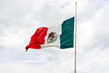 Mexican flag waving on the flagpole with white cloudy sky, space for copy.