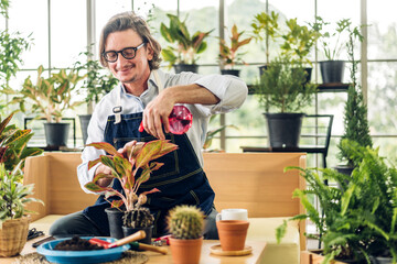 Happy gardener senior old eldery man looking at young plant watering and gardening with potted...