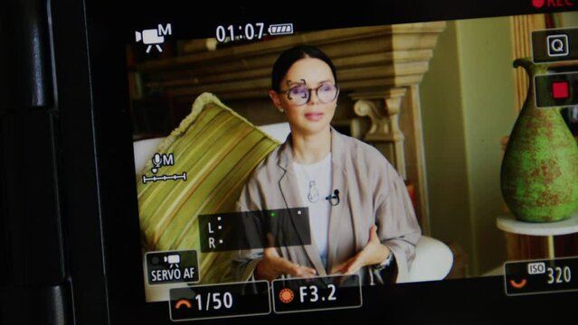 Close-up of caucasian, brunette woman in glasses within charming interior. Video recording of a lady in smart outfit as seen through camera screen. High quality 4k footage