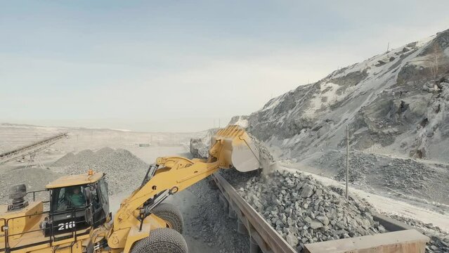 FPV drone view of A big yellow Wheel loader in a quarry is loading wagons with rubble
