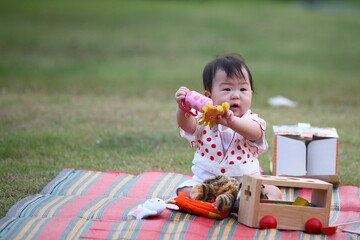 An Asian baby is sitting on colorful mat showing her a pink toy with many toys surrounding her.