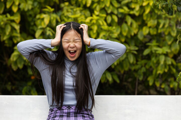 An Asia girl is screaming with 2 hands touching her head in natural light.